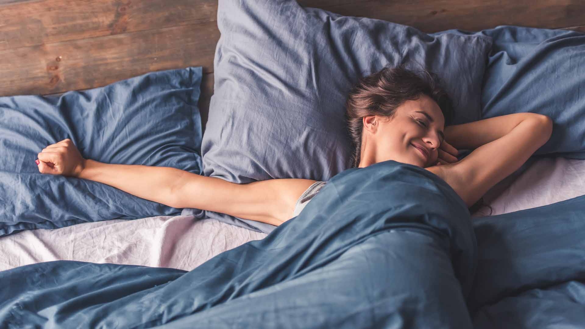 Beautiful young woman is stretching and smiling while lying in bed in the morning