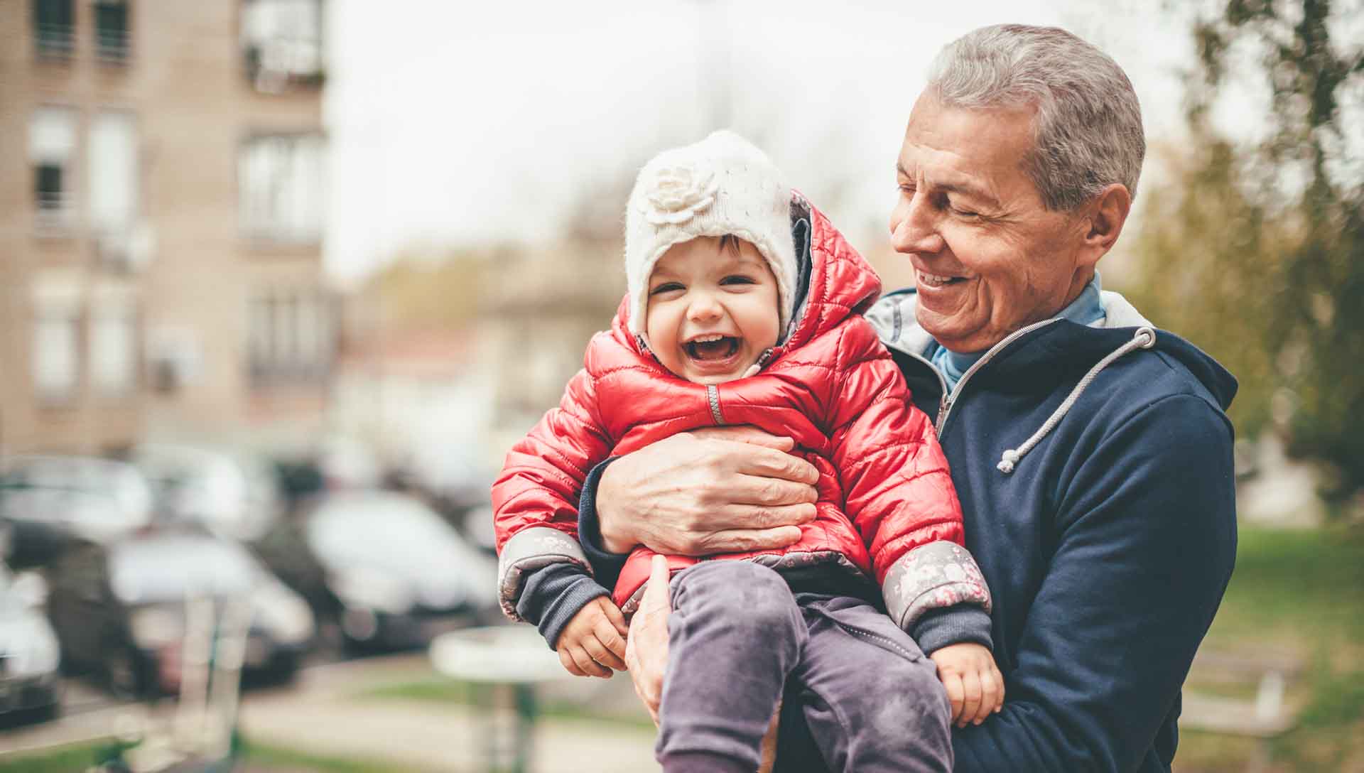 A photo of a playful grandfather and granddaughter. They are casually dressed and playing in the park. The grandfather is holding both kids in his arms.