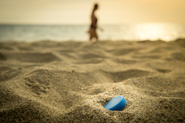 One unrecognisable woman is taking a vacation sunset walk on an idyllic beach.  In the foreground is a single use Plastic water bottle top, in the otherwise pristine sand.  Seemingly harmless, it represents the massive environmental issue that is Global Ocean Pollution.  Plastic in the Ocean is said to be one of the largest threats to our ocean ecosystems.  Over 8 million tonnes is dumped in the Ocean every year.  Discarded, abandoned or obsolete items which become dangerous garbage, is responsible for the deaths of huge amounts of Marine Life every year, through entanglement and consumption.  The location here is Ko Lanta, Krabi, Thailand.