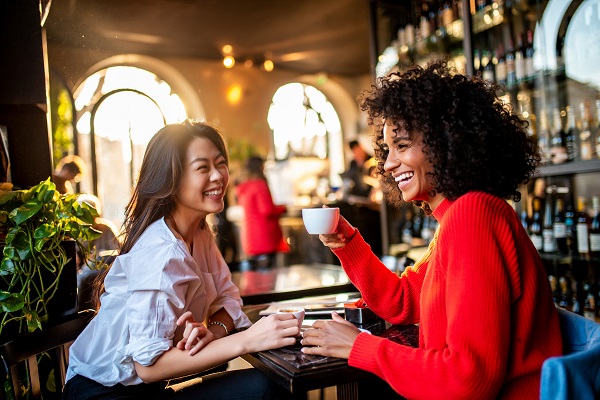 Two smiling female friends having a coffee at the bar