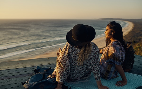 Two young friends watching the sun set over the beach below