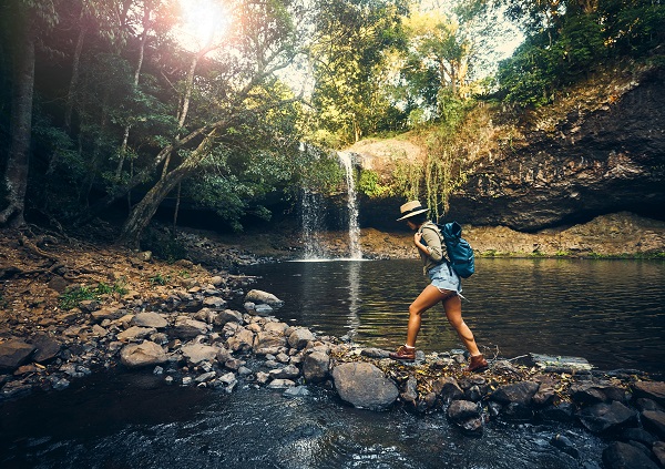 A female traveler makes her way along a stone path at a swimming hole