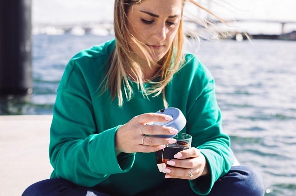 A woman sitting outside opening a drink