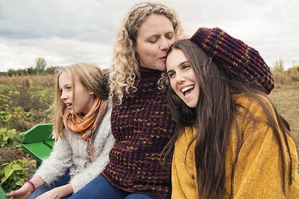 Mother and teenage daughters strolling in trailer in field. Day is ending, and it's time to go back home. Everybody is wearing warm wool sweater. Mother kiss her eldest daughter on the head. Horizontal waist up outdoors shot with copy space. This was taken in Quebec, Canada.