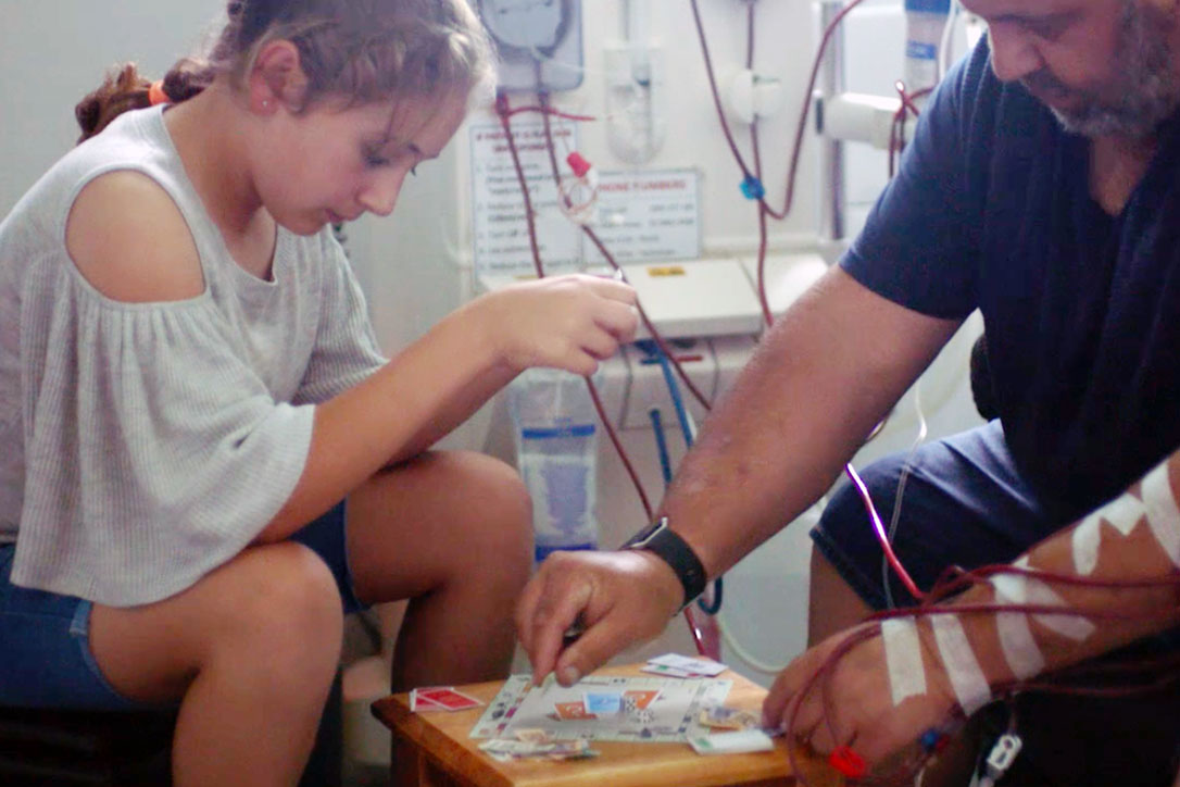 Man plays a board game with a girl in hospital receiving dialysis