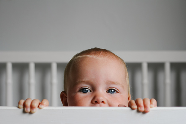 An awake baby looking over the bars of their cot