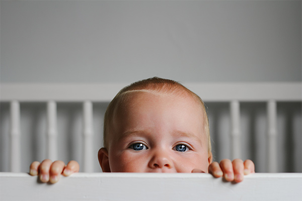 An awake baby looking over the bars of their cot An awake baby looking over the bars of their cot