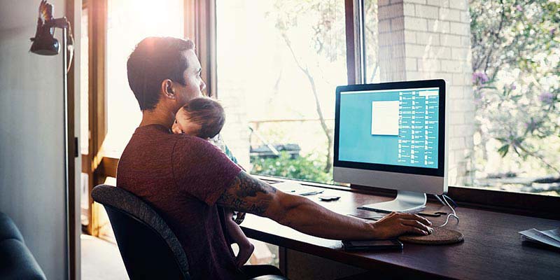 A dad cuddling his newborn while working