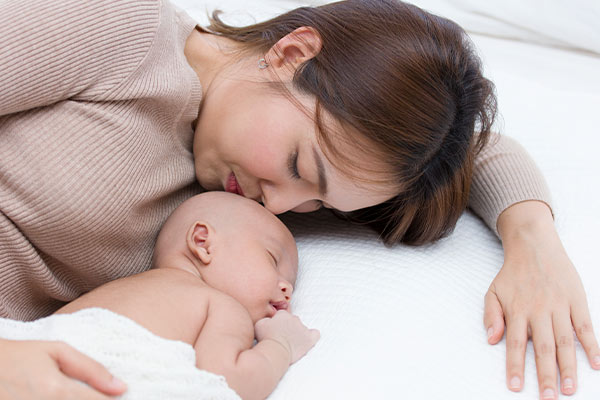 A mother lying next to her sleeping newborn