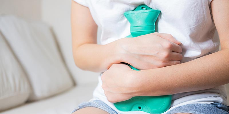 A woman holding a hot water bottle on her stomach