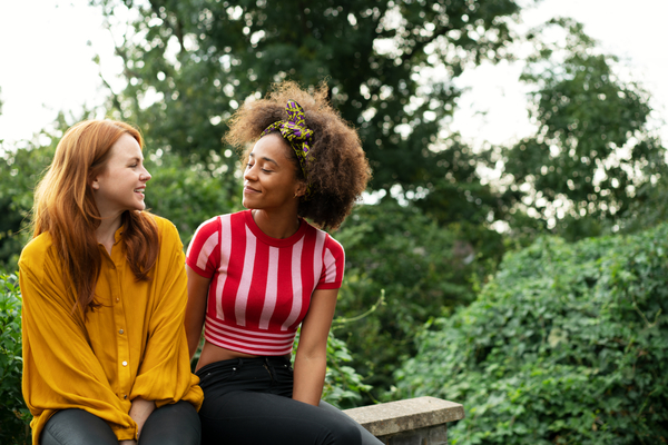 Two girls sitting on a wall smiling together 