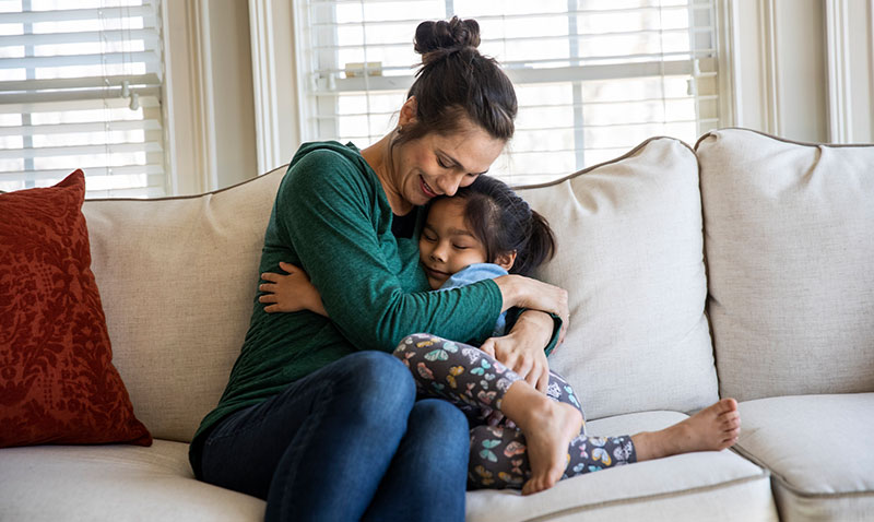 mother hugs young daughter on sofa