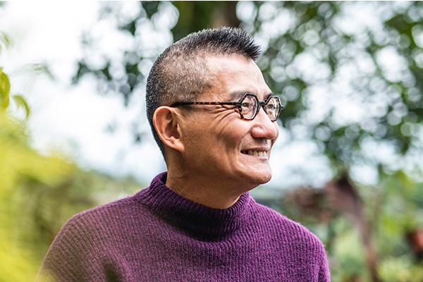 older person smiling while standing amongst the outdoors