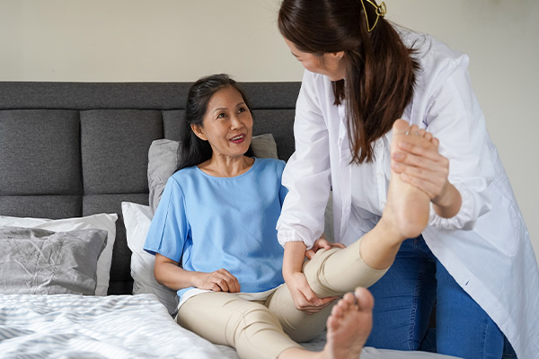 patient sitting on a bed while a physio checks the patient's leg