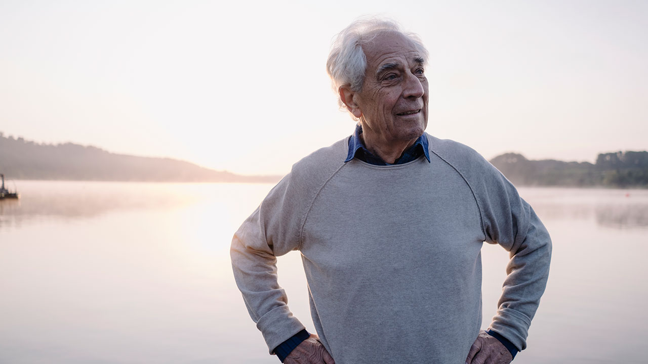 man with grey hair standing in front of a lake