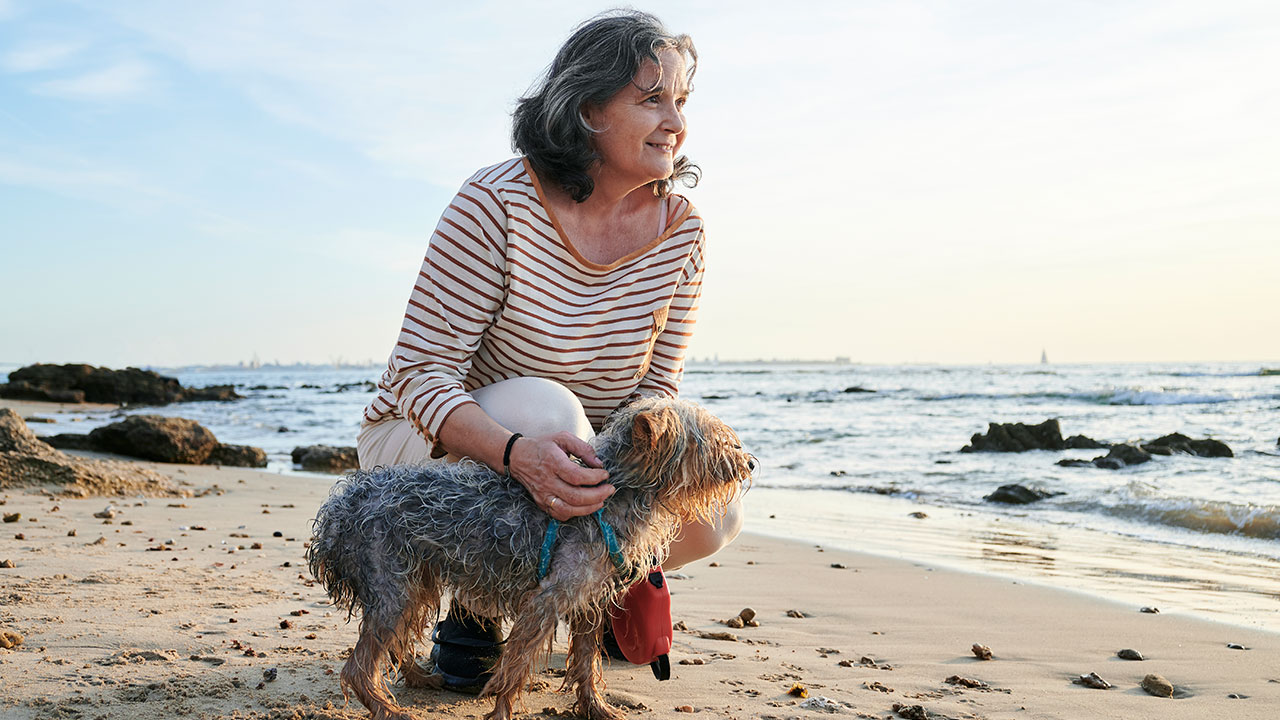 woman crouching with dog at the beach