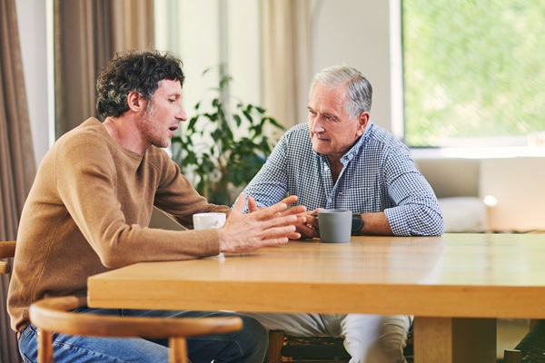 Mature man and his elderly father having coffee and a chat at home