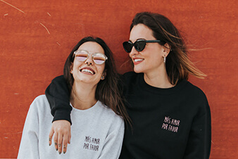 Two women leaning against an orange wall together Two women leaning against an orange wall together