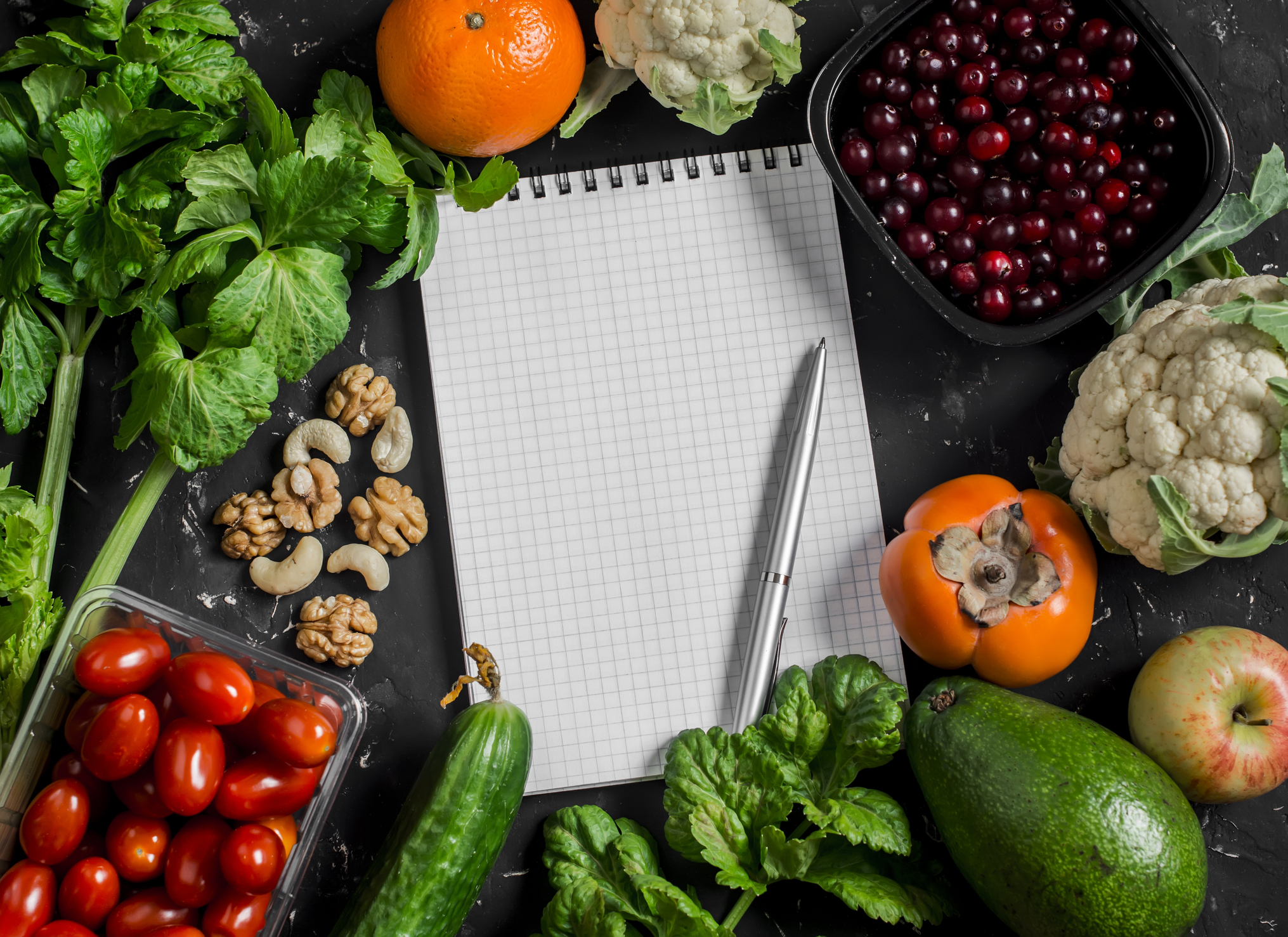 Food background. Fresh vegetables, fruits and blank notepad on a dark background. Concept of healthy eating, diet and planning