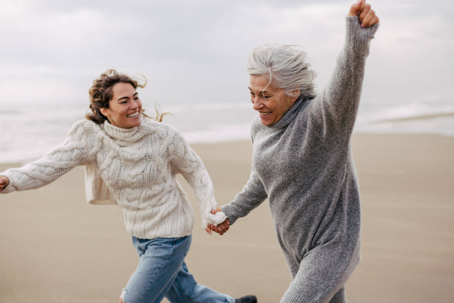 two women walk and celebrate along a windswept beach. Regular exercise can help with the management of osteoarthritis